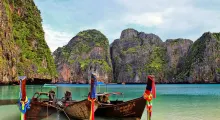 Traditional longtail boats moored in a serene bay surrounded by cliffs in Phuket, Thailand.