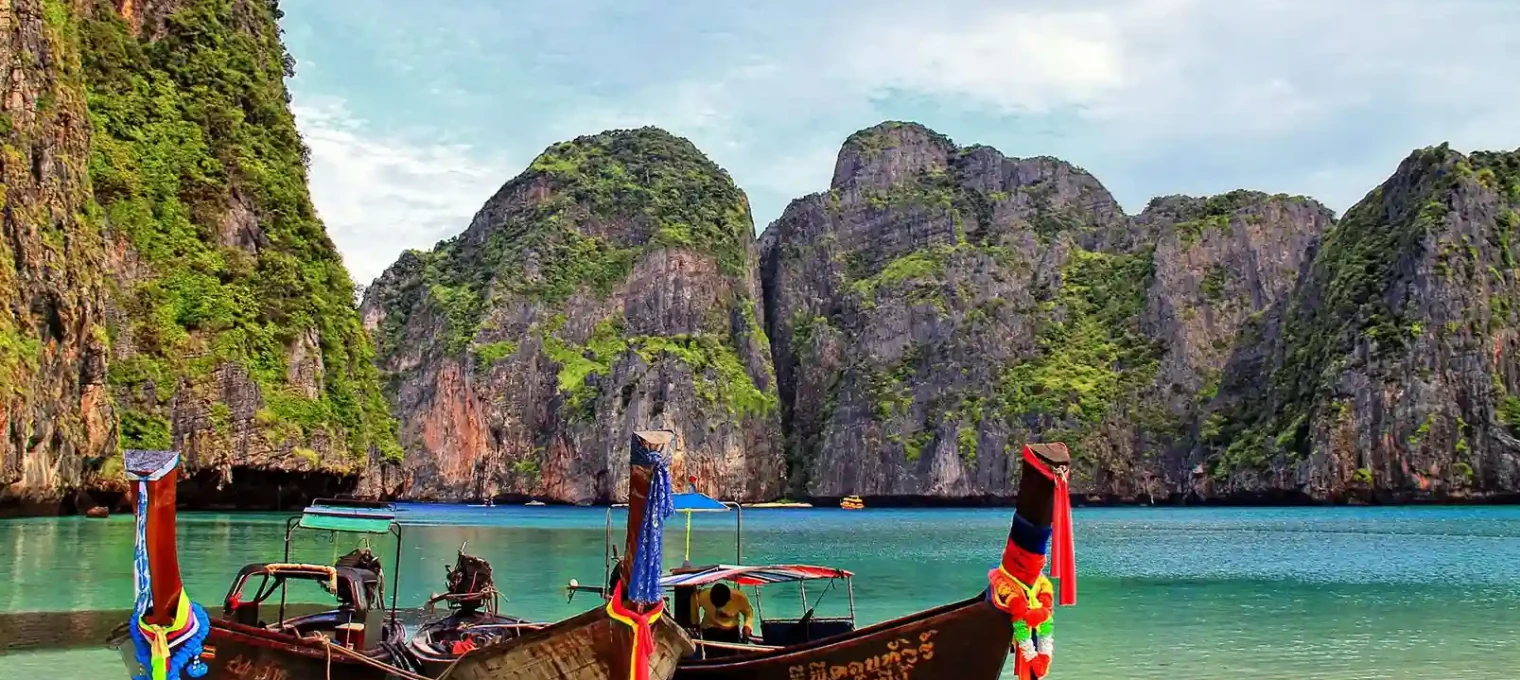 Traditional longtail boats moored in a serene bay surrounded by cliffs in Phuket, Thailand.