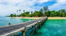 Wooden pier extending into clear turquoise water surrounded by lush greenery in Phuket.