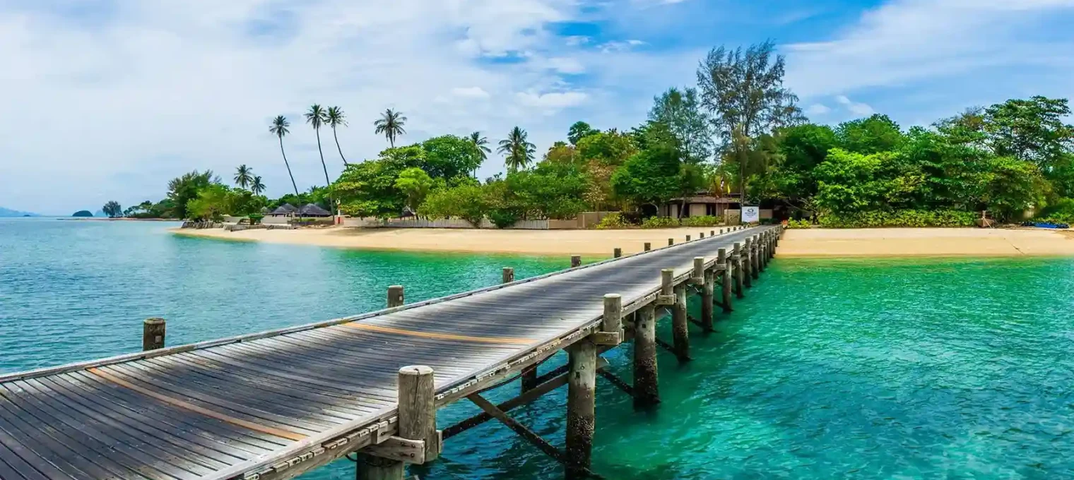 Wooden pier extending into clear turquoise water surrounded by lush greenery in Phuket.