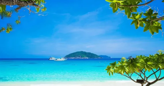 Tropical beach view in Phuket with clear blue water and an island in the distance.