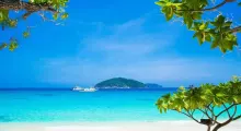 Tropical beach view in Phuket with clear blue water and an island in the distance.