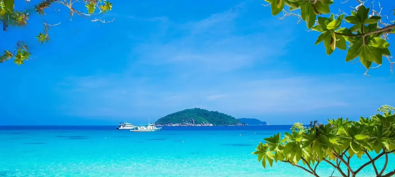 Tropical beach view in Phuket with clear blue water and an island in the distance.