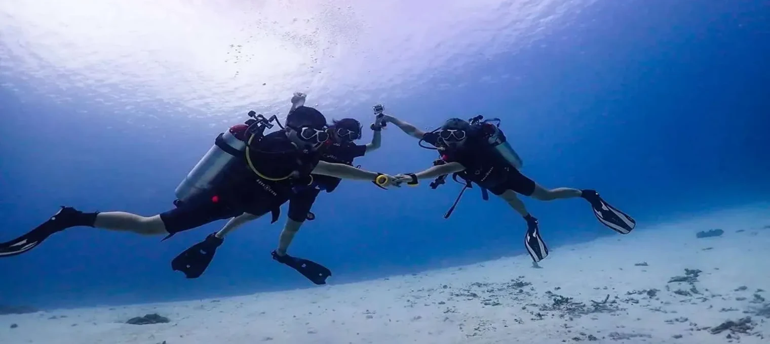 Three divers in snorkeling gear explore the underwater scenery in Phuket's clear waters.