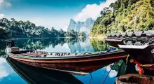 A tranquil scene of wooden boats on a calm lake surrounded by lush greenery and mountains in Phuket.