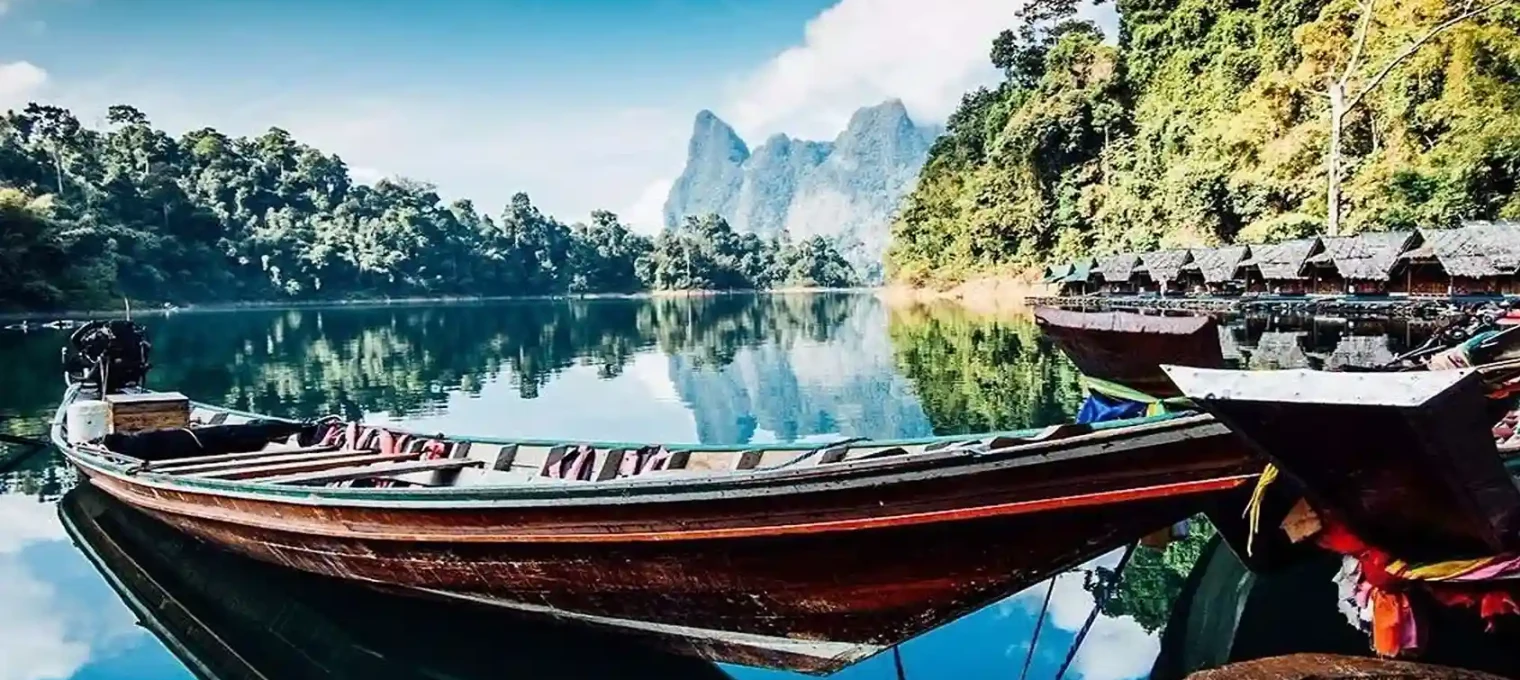 A tranquil scene of wooden boats on a calm lake surrounded by lush greenery and mountains in Phuket.