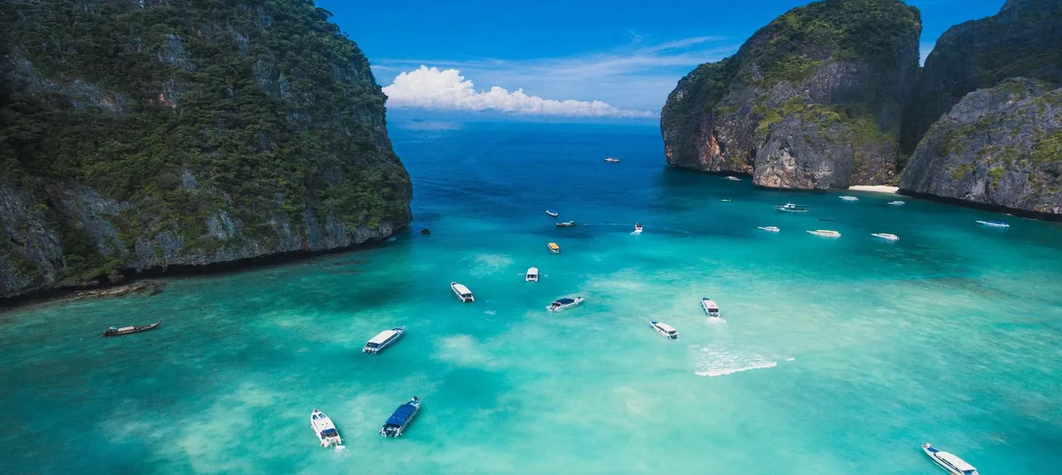 Aerial view of turquoise waters and boats near rocky cliffs in Phuket, Thailand.