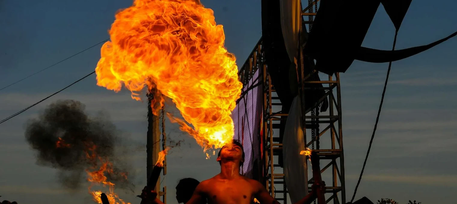 Fire performer breathing fire during a sunset show in Phuket. Spectators in the background.