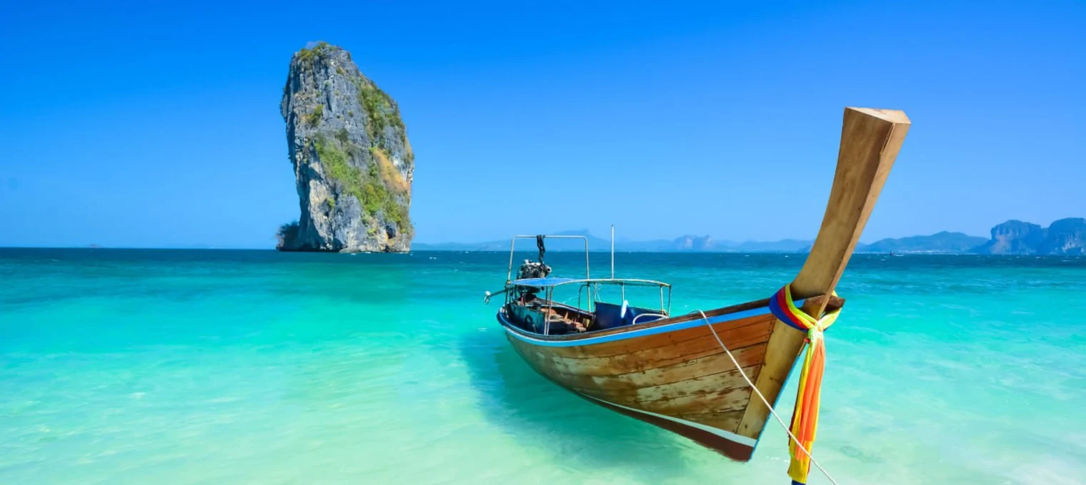 Long-tail boat anchored in clear turquoise waters near a rock formation in Phuket.