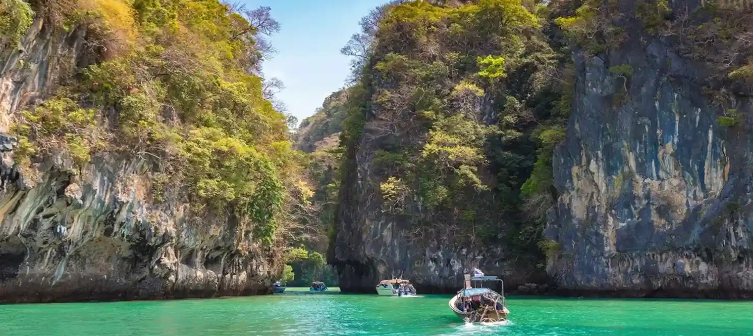 Scenic view of turquoise waters and limestone cliffs in Phuket, Thailand, with boats.
