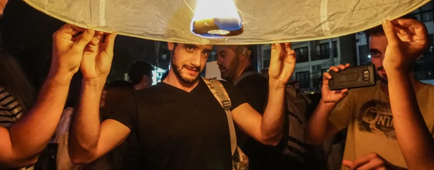 A man holds a flaming sky lantern at a festive event in Phuket, surrounded by onlookers.
