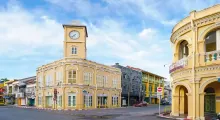 Colorful historic buildings with a clock tower in Phuket, Thailand under a bright sky.