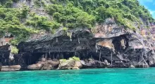 Lush green cliffs surround a cave near turquoise waters in Phuket, Thailand.