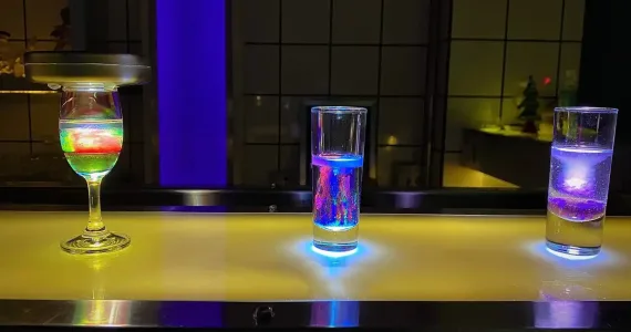 Three illuminated glasses on a bar counter in Phuket, showcasing colorful drinks.