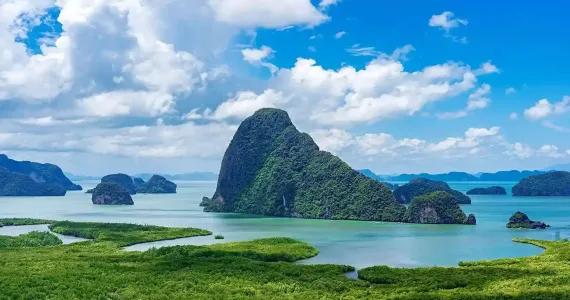 Lush green islands and cliffs rise from turquoise waters under a blue sky in Phuket.
