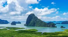 Lush green islands and cliffs rise from turquoise waters under a blue sky in Phuket.