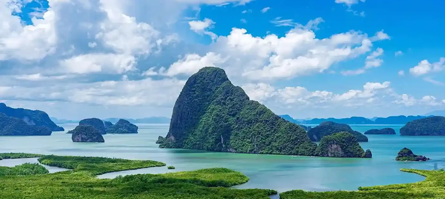 Lush green islands and cliffs rise from turquoise waters under a blue sky in Phuket.