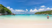 Sunny beach in Phuket with clear turquoise water, white sand, and people enjoying the sun.
