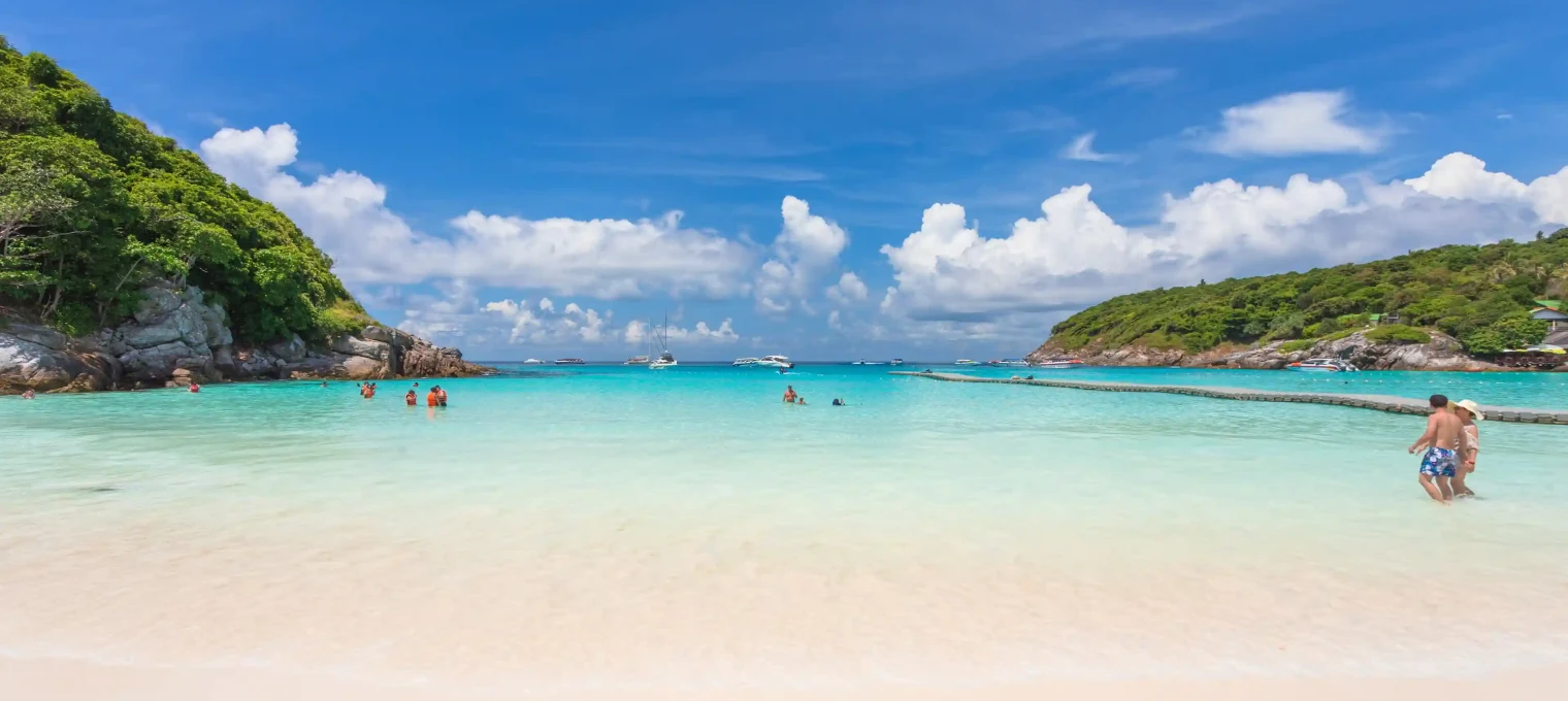 Sunny beach in Phuket with clear turquoise water, white sand, and people enjoying the sun.