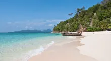 Serene beach in Phuket with clear water, sandy shore, and traditional boats along the coast.