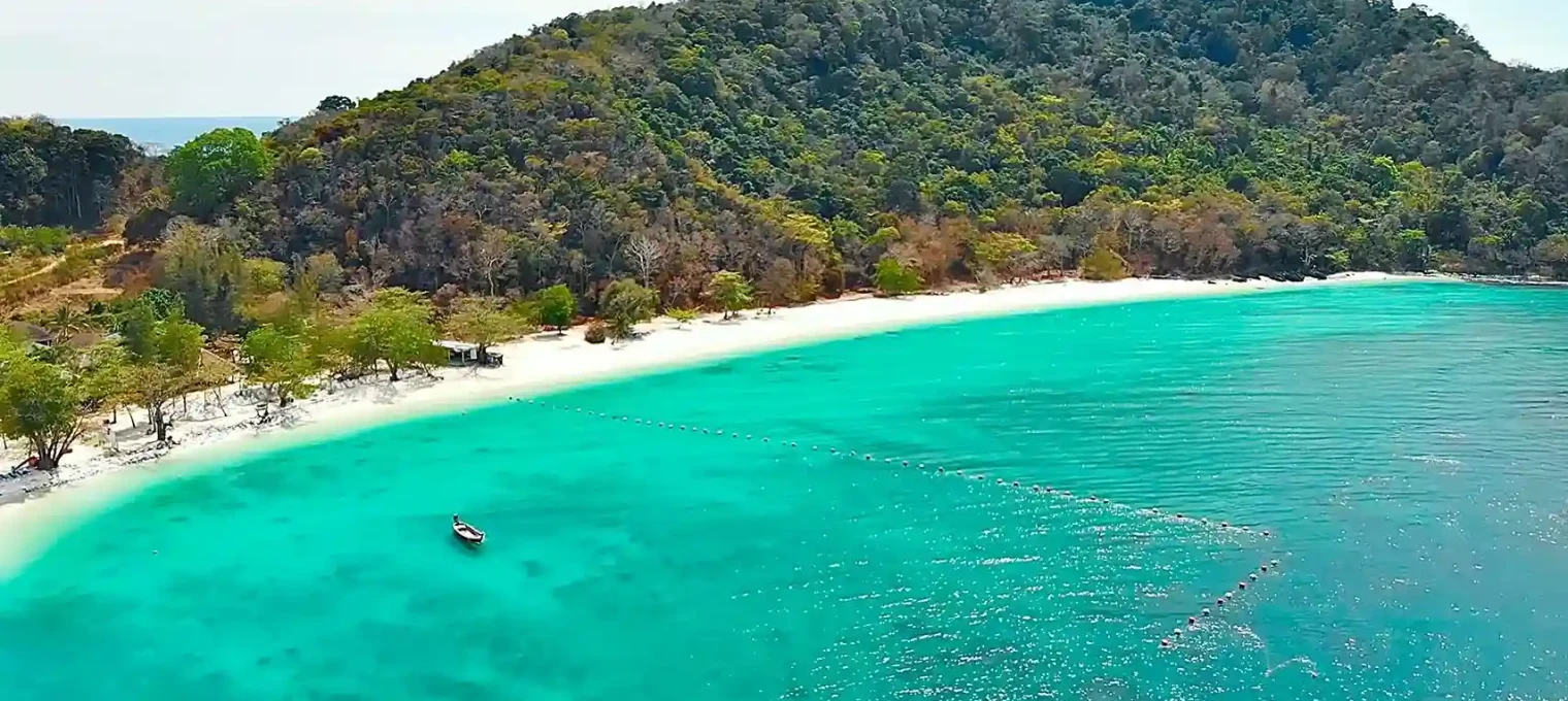 Stunning turquoise waters and white sandy beach in Phuket, surrounded by lush greenery.