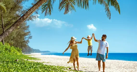 Семья на пляже в Пхукете: родители держат за руки ребенка под пальмами.