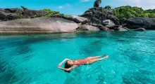 A person swims in clear turquoise water surrounded by rocks in Phuket.