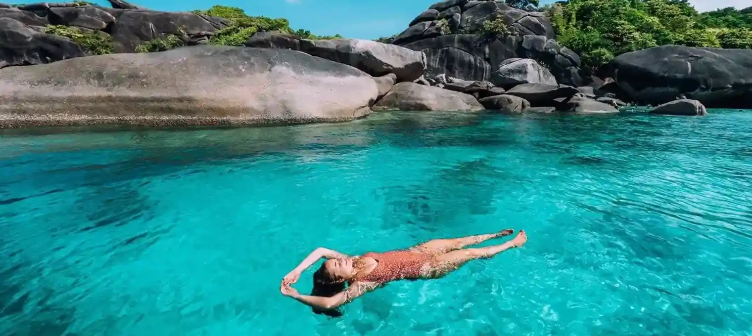 A person swims in clear turquoise water surrounded by rocks in Phuket.