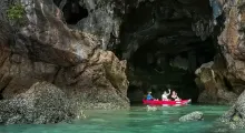 A group of people kayaking through a limestone cave in Phuket's clear blue waters.