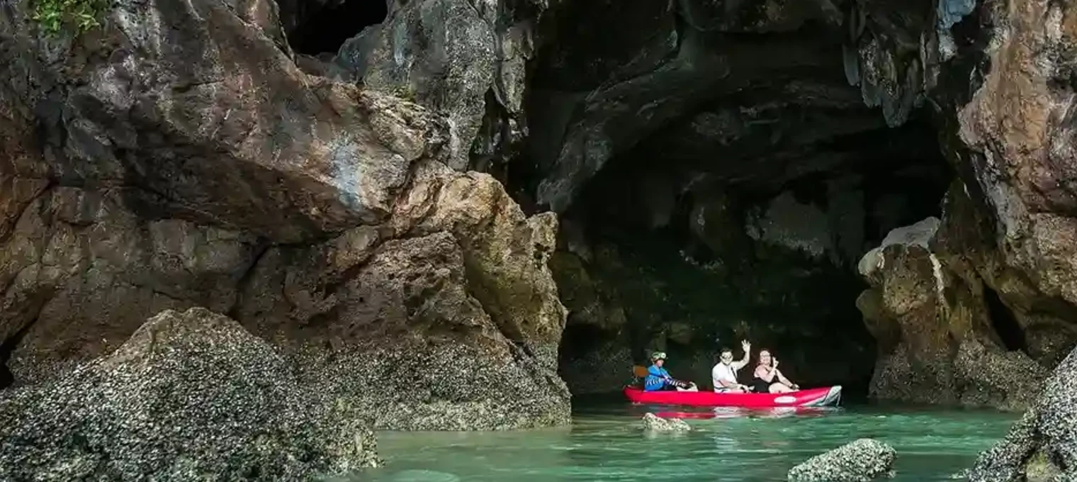 A group of people kayaking through a limestone cave in Phuket's clear blue waters.
