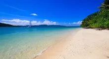 Pristine beach in Phuket with clear water, gentle waves, and a distant sailboat.