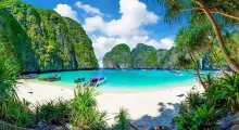 Tropical beach in Phuket with clear water, boats, lush greenery, and dramatic cliffs.