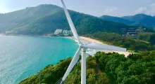 Aerial view of a wind turbine overlooking a beach and lush green hills in Phuket.